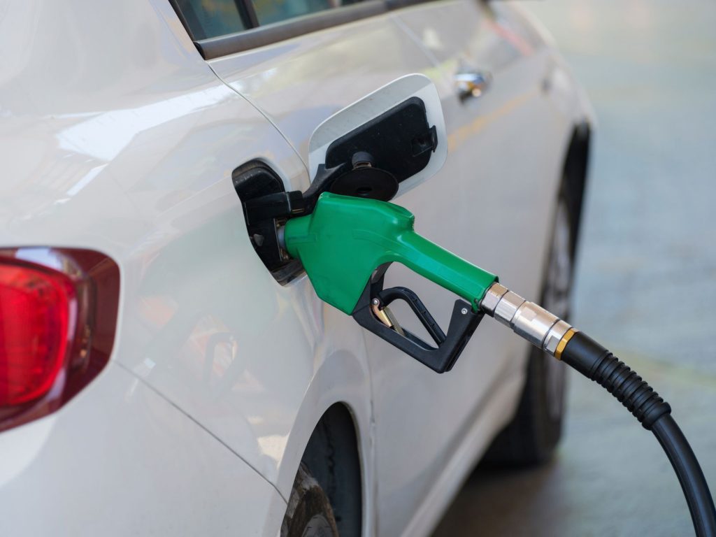 Governo anuncia medidas para conter alta dos combustíveis e mantém subsídio ao diesel Close-up de uma bomba com bico verde abastecendo um carro branco em um posto de combustíveis.